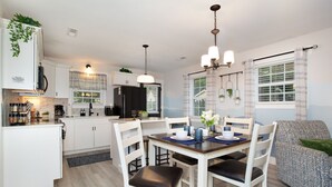 A modern kitchen with white cabinets, a black refrigerator, and a dining area with a wooden table and white chairs.