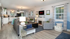 A modern living room with a fireplace, a television, and a kitchen in the background.