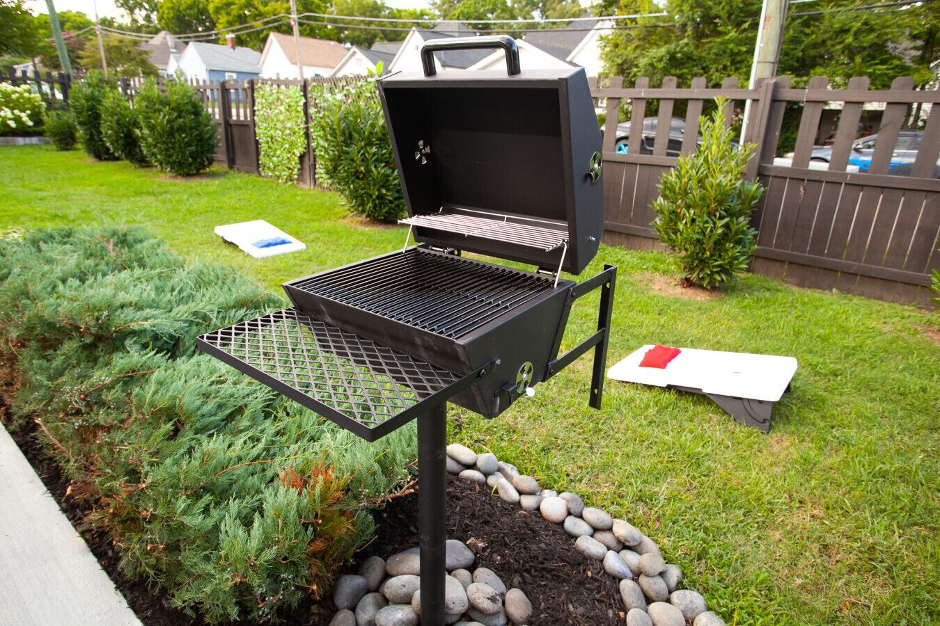 A backyard with a portable grill, a small table, and a garden bed with rocks and plants.