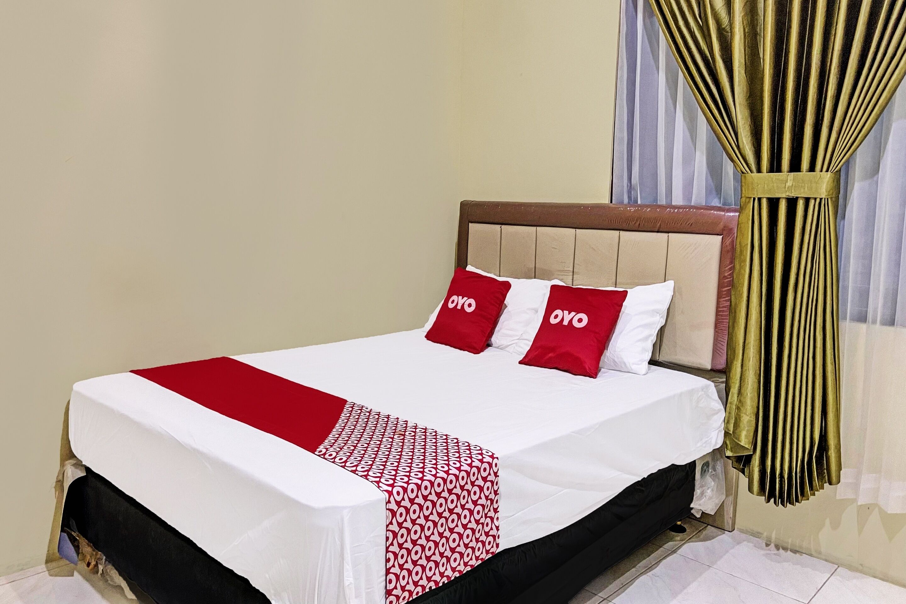 A neatly made bed with a white and red bedspread, two red pillows with "OYO" branding, and a wooden headboard.