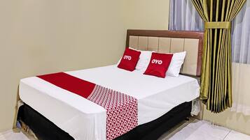 A neatly made bed with a white and red bedspread, two red pillows with "OYO" branding, and a wooden headboard.