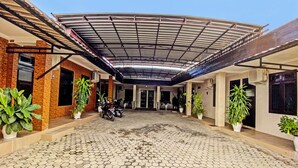 Un espace extérieur abrité, doté d’un sol carrelé, de plantes en pot et d’une moto garée au centre.