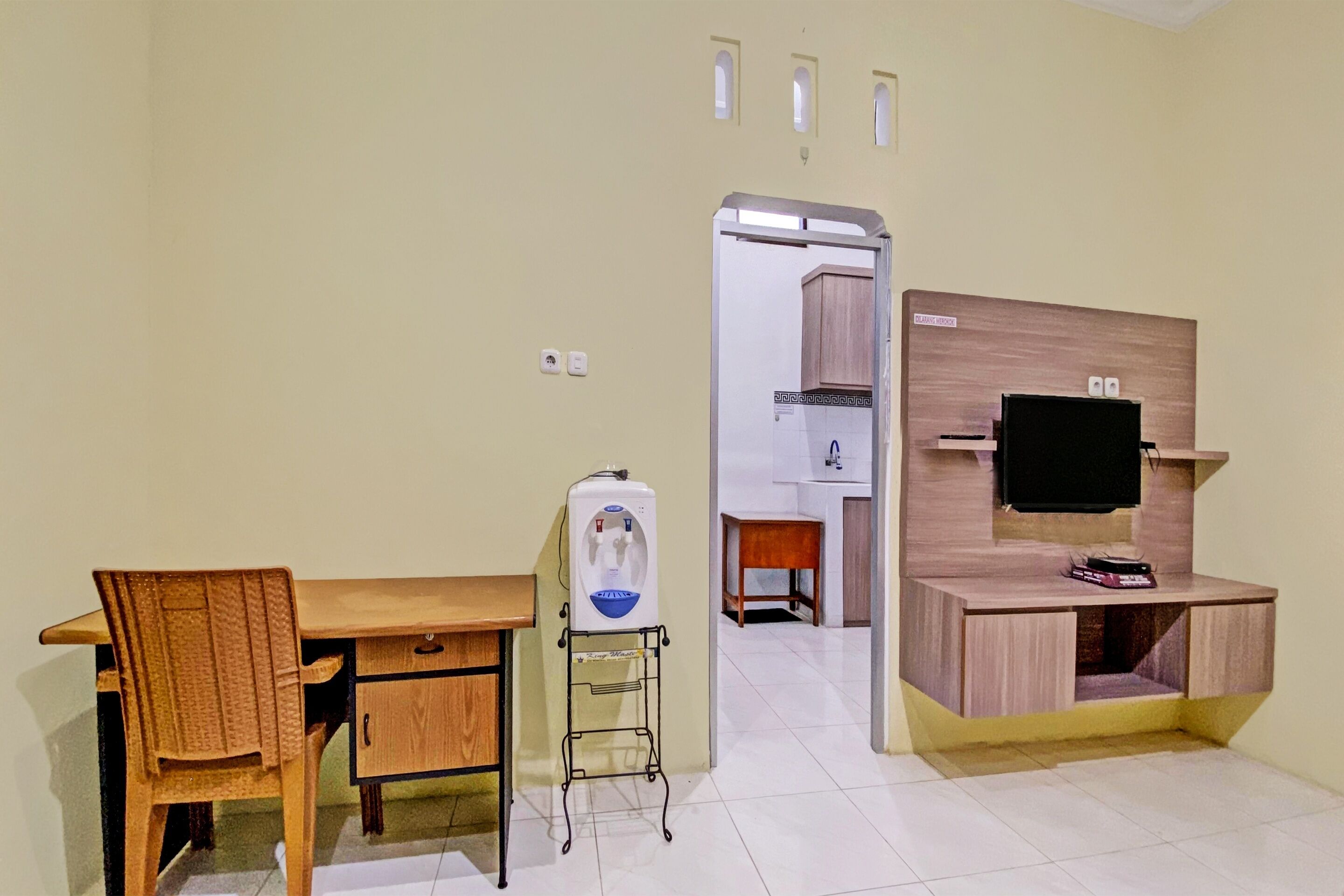 A room with a wooden desk, a chair, a water dispenser, a television, and a small cabinet.