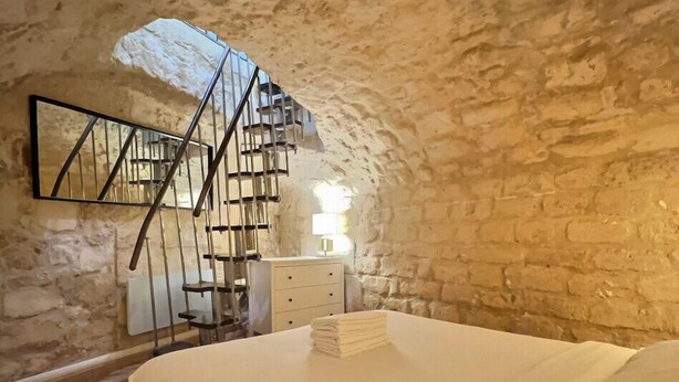 A bedroom with a bed, a dresser, a mirror, and a spiral staircase against a stone wall. - A unique duplex in the heart of Montorgueil (Paris)