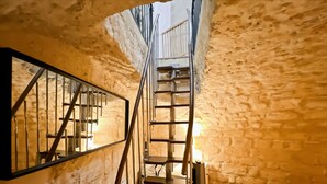 A narrow staircase with metal railings leading to an upper level, surrounded by textured stone walls. - A unique duplex in the heart of Montorgueil (Paris)