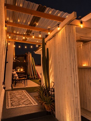 An outdoor patio area with a wooden pergola, string lights, a cactus, and a table with chairs. - The Zen Den (Venice)