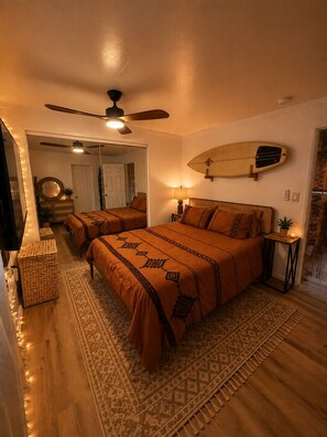 A bedroom with a bed, a ceiling fan, a surfboard on the wall, and a small table with a lamp. - The Zen Den (Venice)