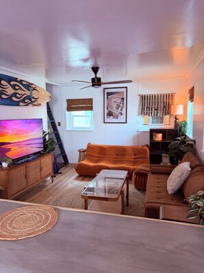 A living room with a sofa, a coffee table, a TV, and a ceiling fan. - The Zen Den (Venice)