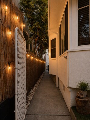 A narrow pathway flanked by a bamboo fence and a building with large windows. - The Zen Den (Venice)