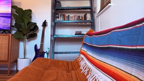 A bedroom with a bed, a bookshelf, a guitar, and a surfboard. - The Zen Den (Venice)