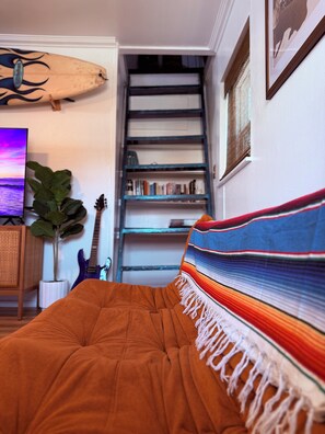 A bedroom with a bed, a bookshelf, a guitar, and a surfboard. - The Zen Den (Venice)