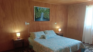 Une chambre à coucher avec un lit, deux lampes de chevet, un tableau accroché au mur et un sol à motifs.