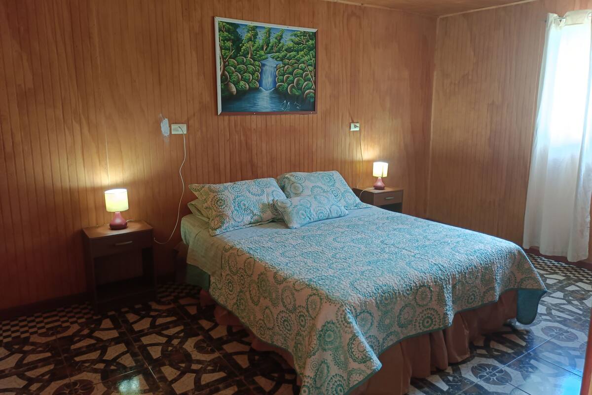 A bedroom with a bed, two bedside lamps, a wall-mounted painting, and a patterned floor.