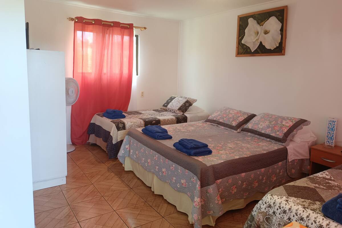 A hotel room with two beds, a red curtain, a fan, and a floral painting on the wall.