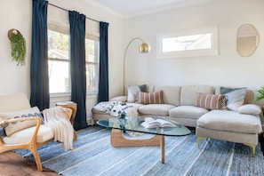 A living room with a beige sofa, a glass coffee table, a wooden chair, and a blue striped rug.