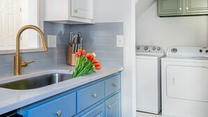 A kitchen with a stainless steel sink, blue cabinets, and a gold faucet. There are two washing machines and a set of knives on the counter. - Rook's Corner (Atlanta)