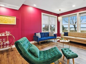 A modern living room with a red accent wall, a blue sofa, a green armchair, and a beige sofa.