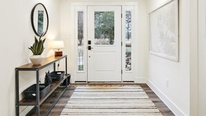 A hallway with a white door, a console table with a lamp, a potted plant, and a framed picture on the wall.