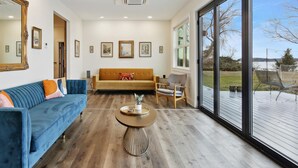 A spacious living room with a large window, a ceiling fan, and a wooden floor.