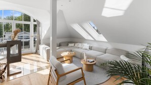 Ein modernes Wohnzimmer mit einer großen, L-förmigen Eckcouch, einem Glastisch und einem Holzstuhl.