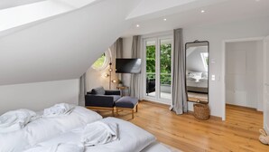 Ein modernes Schlafzimmer mit einem großen Bett, einem Fernseher, einer Couch und Blick auf Grünfläche.