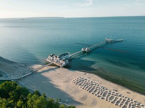Un hôtel situé sur la côte, doté d’une jetée qui s’avance dans la mer, d’une plage de sable et d’une vue dégagée sur l’océan.