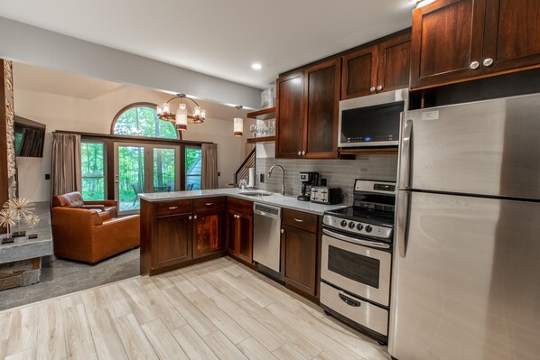 A modern kitchen with wooden cabinets, stainless steel appliances, and a large window offering a view of the outdoors.