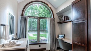 Une salle de bain dotée d’une grande fenêtre en arc de cercle, d’un meuble-lavabo avec un miroir, d’une baignoire et d’une étagère ornée d’objets décoratifs.