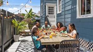 Eine Familie speist draußen an einem Tisch mit Stühlen und einer Brüstung.