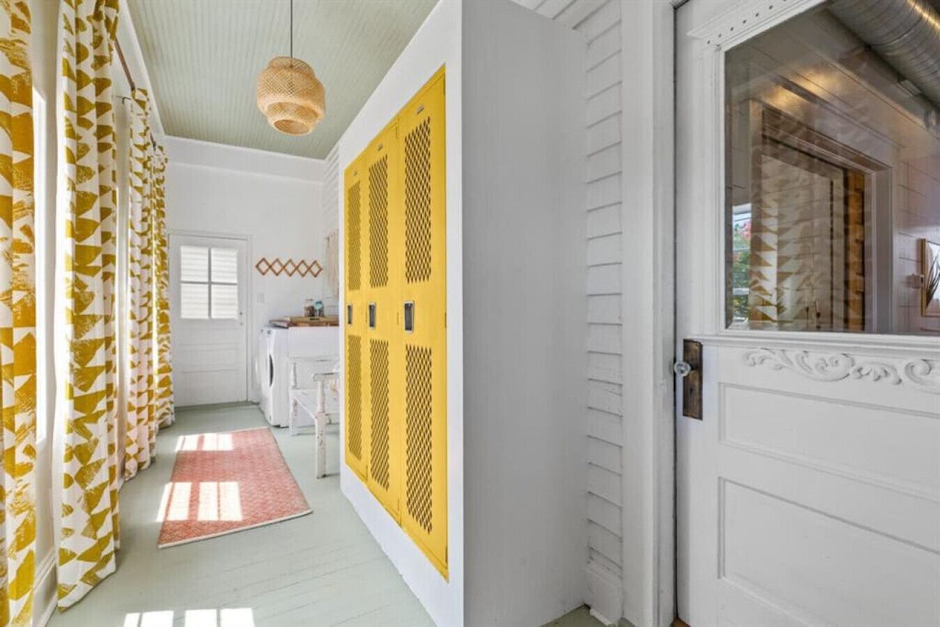 Un corridoio con tende a motivi decorativi, una porta gialla con motivo geometrico e una porta bianca con pannello di vetro decorativo.