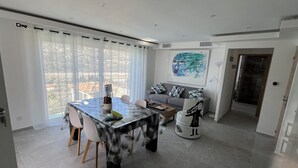 A modern living room with a dining area, large windows, a grey sofa set, and a painting on the wall. - Charming Villa (Saint-Martin-du-Var)