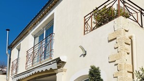 A two-story building with a balcony, potted plants, and a stone wall. - Charming Villa (Saint-Martin-du-Var)