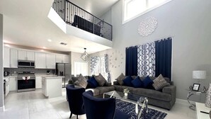 A spacious living area with a grey sofa, two armchairs, and a coffee table. A kitchen with white cabinets and a built-in oven is visible in the background. - Luxury Villa Near Disney 6 Bd Home with Private Pool and Resort (Davenport)