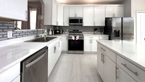 A modern kitchen with white cabinets, stainless steel appliances, and a tiled backsplash. - Luxury Villa Near Disney 6 Bd Home with Private Pool and Resort (Davenport)