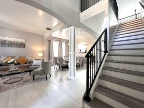 A spacious living area with a staircase leading to an upper floor. - Luxury Villa Near Disney 6 Bd Home with Private Pool and Resort (Davenport)