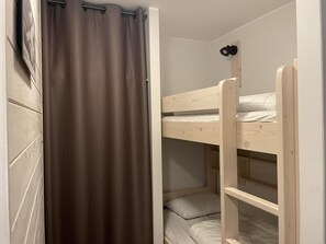 A bunk bed room with a curtain, wooden walls, and a shelf unit.