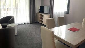 A hotel room with a dining table, four chairs, a TV on a wooden cabinet, and a large window with sheer curtains. - 150m from ski slopes, 3rd floor, swimming pool, terrace, tv, ski locker, 49m², Gourette (Eaux-Bonnes)