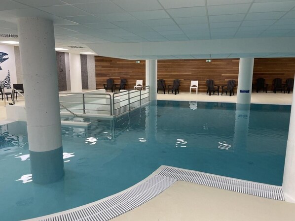 An indoor swimming pool with a wooden wall and seating area.