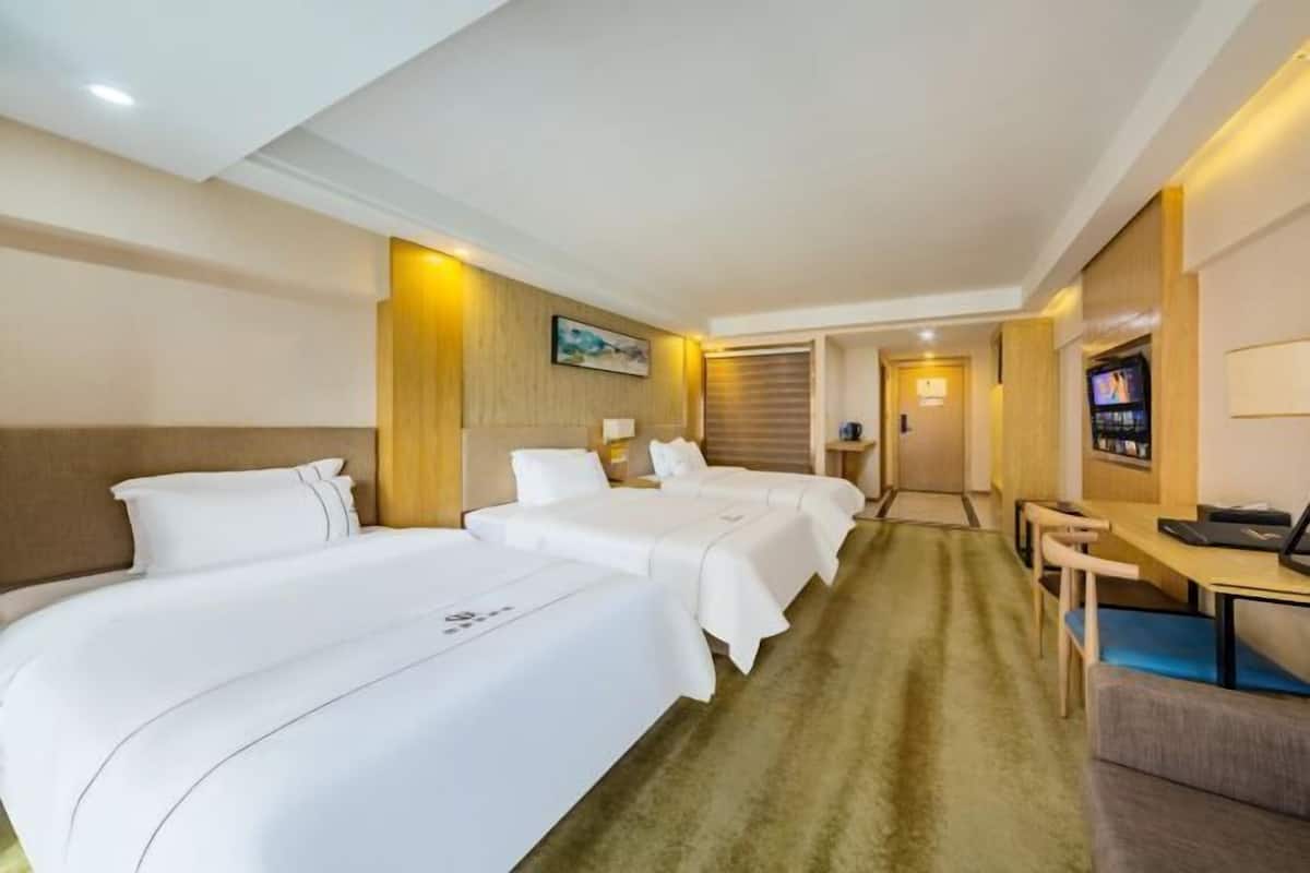 A hotel room with three beds, a desk, a TV, and a carpeted floor.