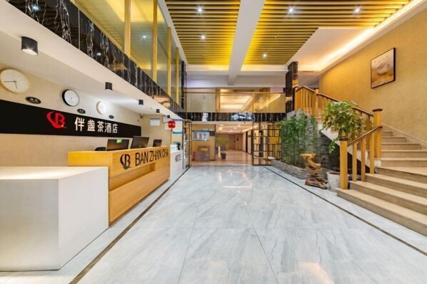 A hotel reception area with a modern design, featuring a reception desk, a staircase, and a large plant. - Banzhancha Hotel (Chongqing)