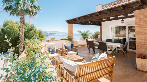 Une terrasse avec des meubles d’extérieur, un palmier et une vue sur l’océan.