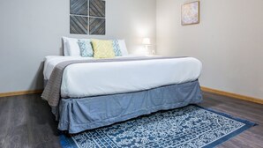 A bedroom with a bed, a nightstand, a lamp, and a blue patterned rug. - 7th Heaven Guesthouse (Hermann)