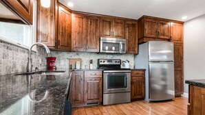A modern kitchen with wooden cabinets, stainless steel appliances, and a granite countertop. - 7th Heaven Guesthouse (Hermann)