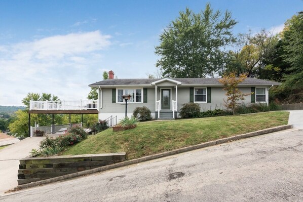 A single-story house with a front porch, a small deck, and a sloped lawn.
