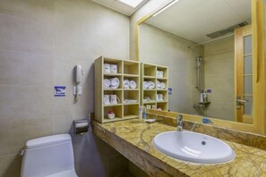 Un baño con lavabo de mármol, inodoro, estante con artículos de aseo y un espejo grande.