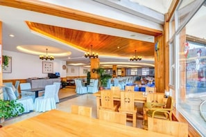 A spacious dining area with wooden tables and chairs, a high ceiling with wooden beams, and pendant lighting. - Shuanglong Hotel (Zhangjiakou)