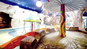 Zona de juegos acuáticos interior con toboganes y una gran estructura tipo paraguas.
