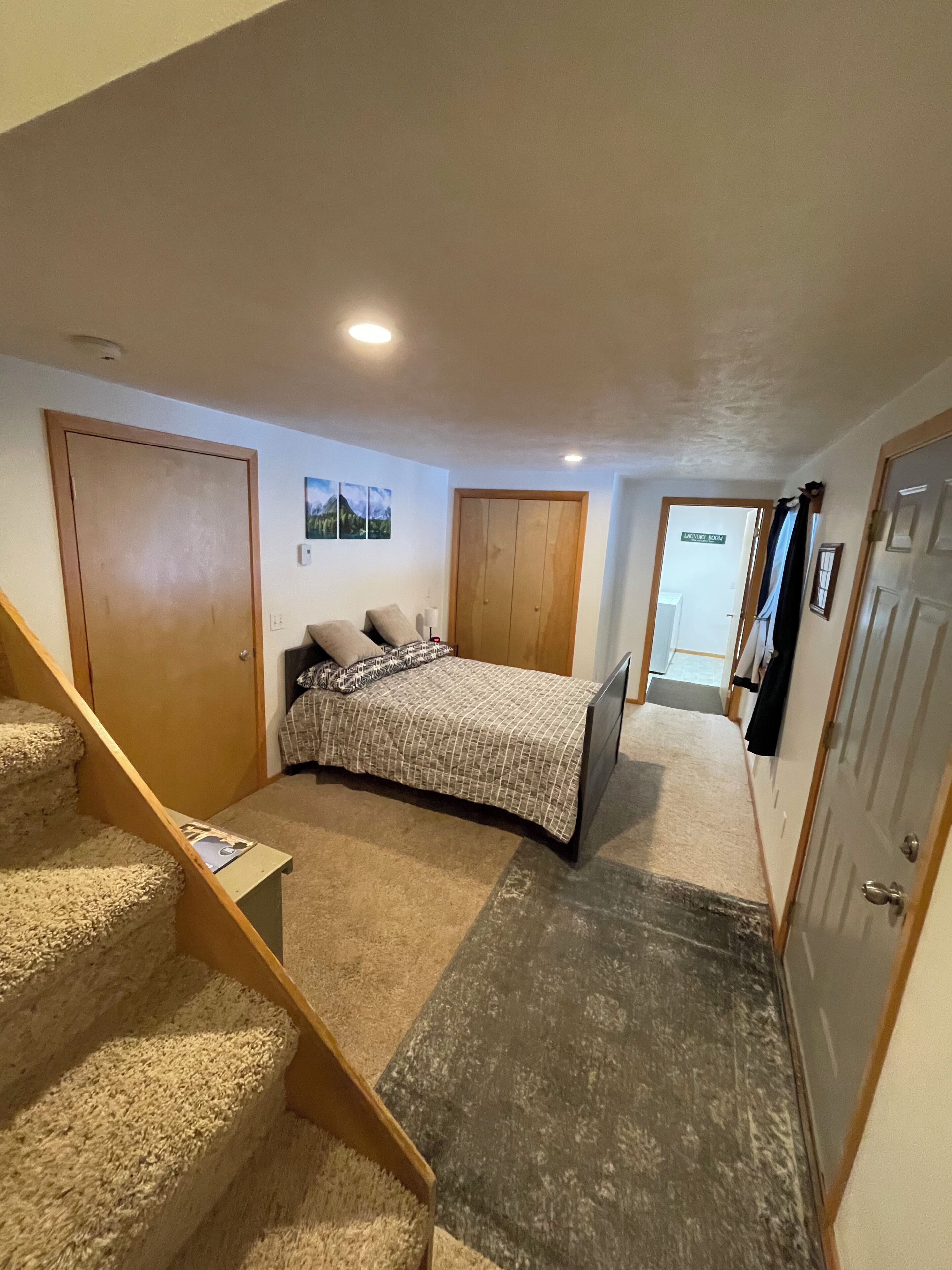 A bedroom with a bed, a staircase, a door, and a hallway leading to another room.