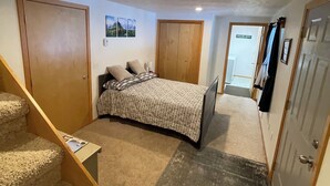 A bedroom with a bed, a staircase, a door, and a hallway leading to another room.