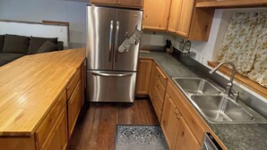 A kitchen with wooden cabinets, a stainless steel refrigerator, a granite countertop, and a patterned rug.